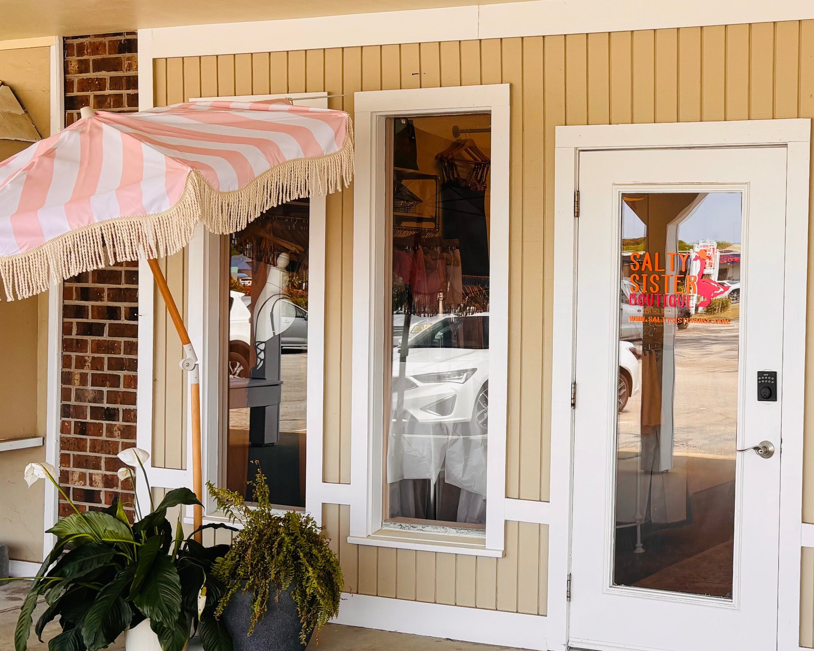 Outdoor seating area with tables, chairs, and a striped umbrella in front of a store entrance.